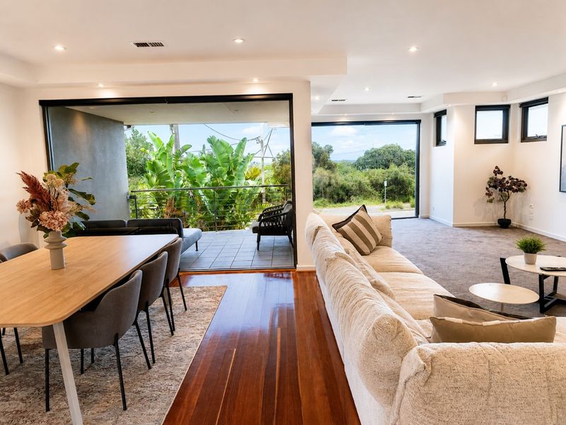 Open-plan living and dining room opening to greenery at Beach Road House